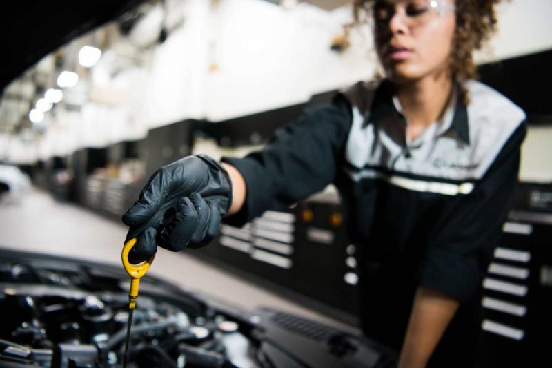 A service technician checks the oil under a vehicle's hood.
