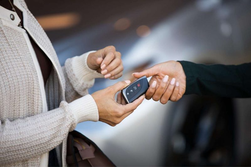 A Lexus salesperson hands keys to a new vehicle over to a guest.