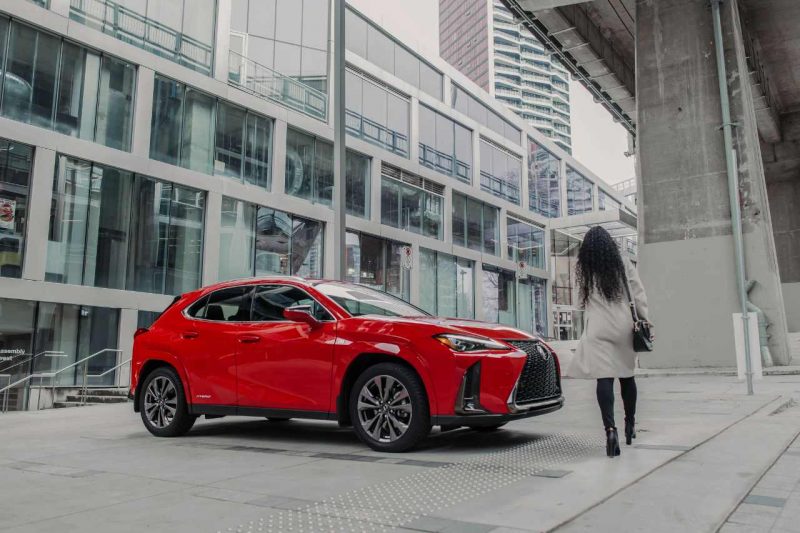 A woman walks towards her Lexus hybrid vehicle in a city setting.