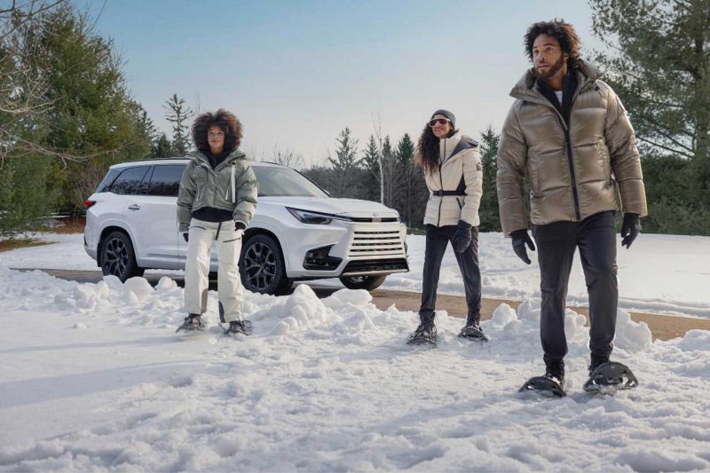 There is a Lexus hybrid SUV parked next to a family playing in the snow.