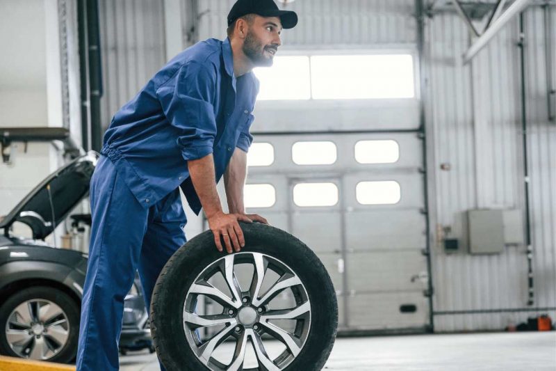 A mechanic rolling a tire around in an auto service center.