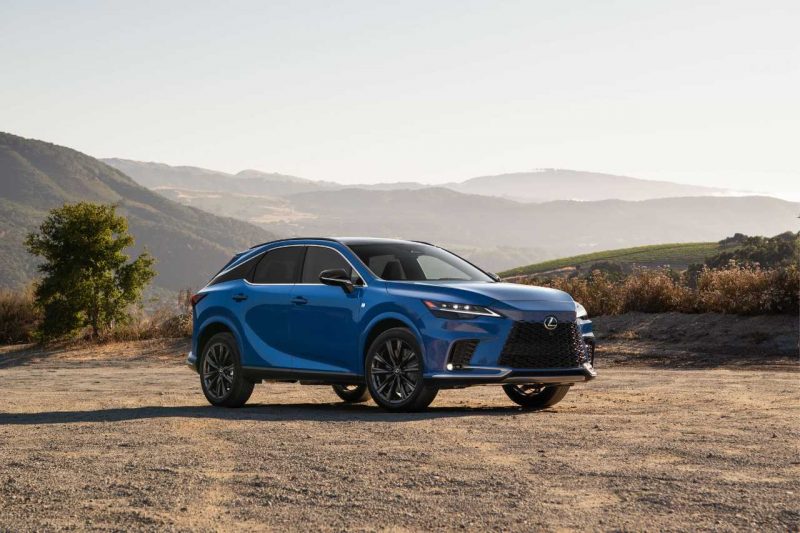 A blue 2024 Lexus RX SUV stands on a dusty dirty road on a sunny day.